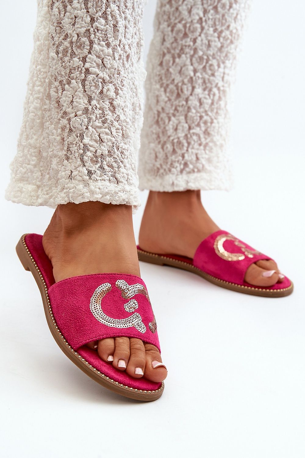 Pink suede flip-flops with sequin designs, paired with white textured pants, showcasing summer style and comfort.