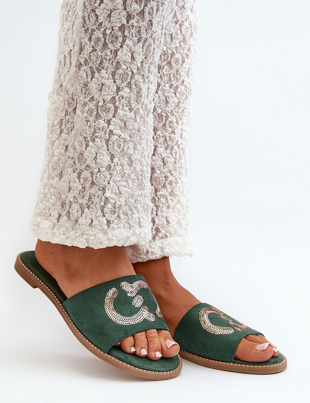 Green suede flip-flops with sequins worn by a person in white lace pants, showcasing style and comfort for summer.