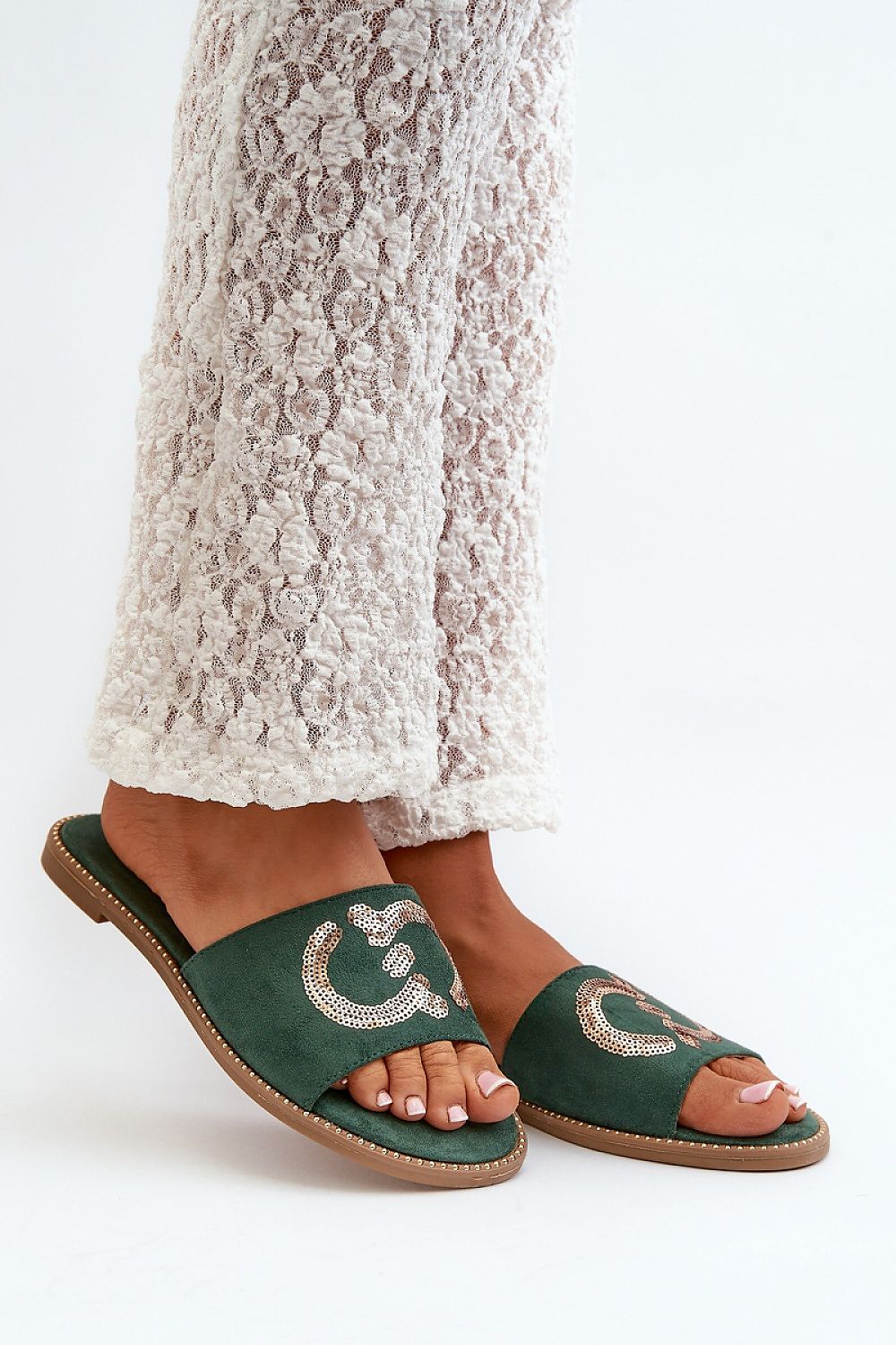 Green suede flip-flops with sequins worn by a person in white lace pants, showcasing style and comfort for summer.