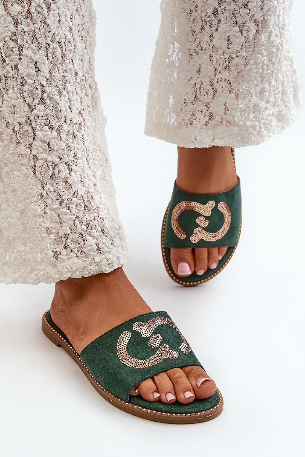 Woman wearing Naerelle Suede Spark Flip-Flops with sequin detail, paired with white lace pants, showcasing a casual summer look.
