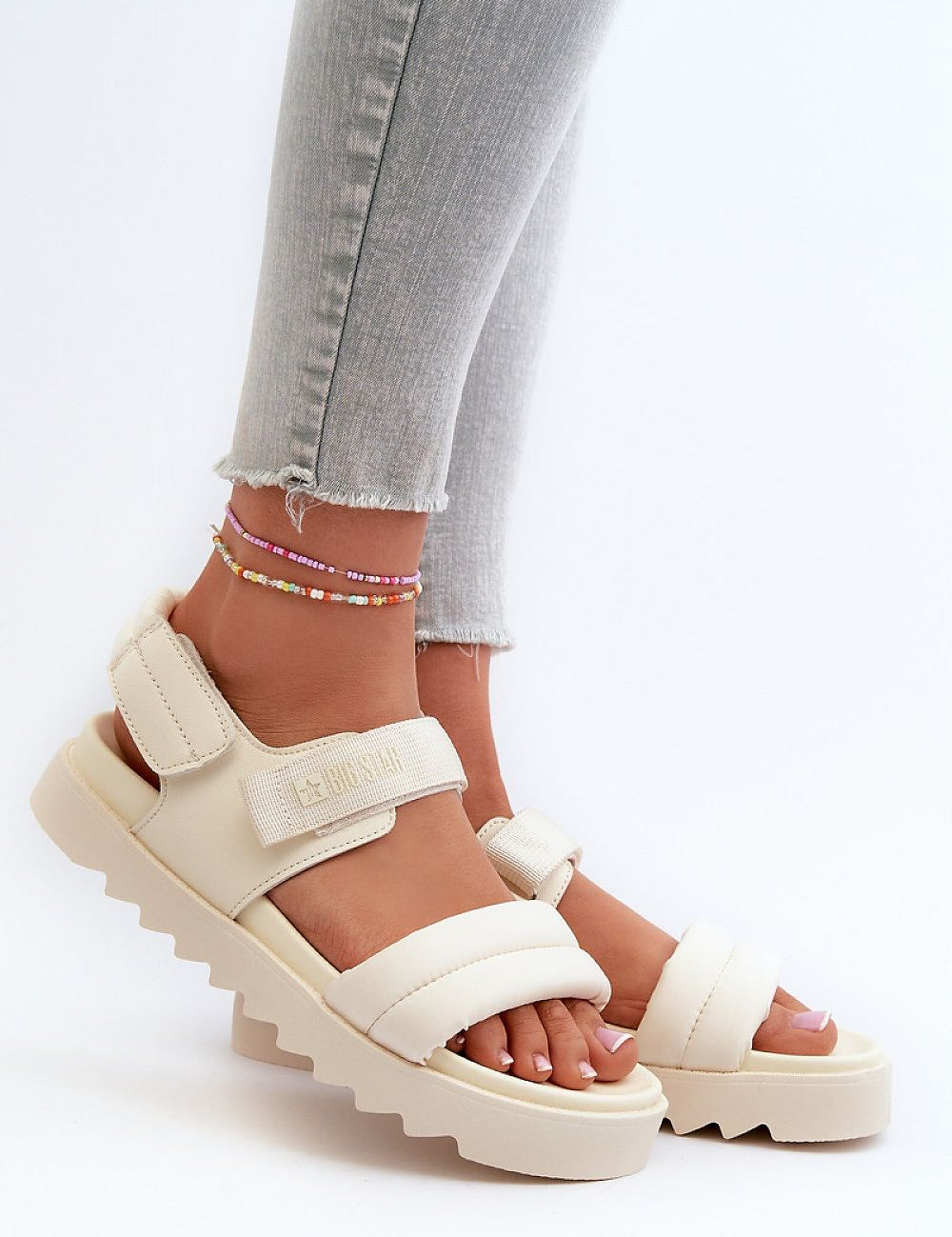 Person wearing Rivexa platform strap sandals with Velcro fastening in beige, paired with grey jeans, showcasing comfort and style.