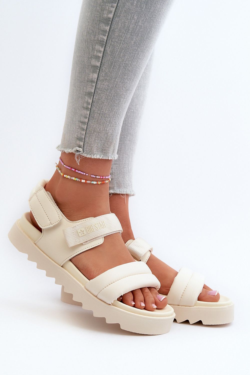 Person wearing Rivexa platform strap sandals with Velcro fastening in beige, paired with grey jeans, showcasing comfort and style.