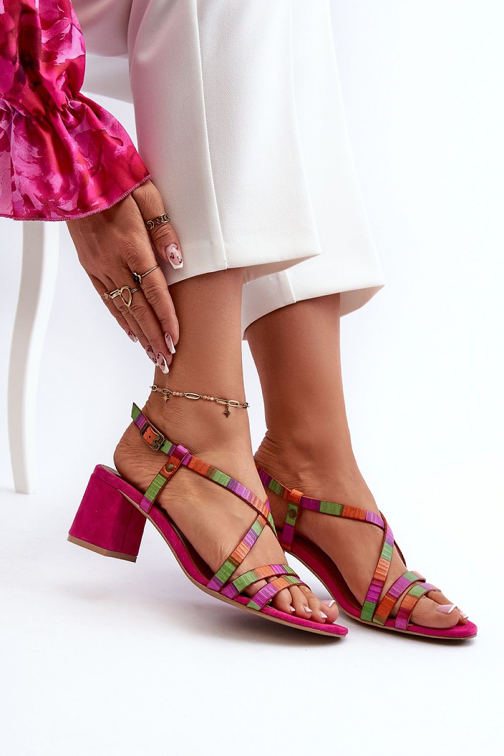 Woman wearing Arceline Leather Strap Sandals in vibrant colors with a mid-height heel, styled with white pants and pink top.