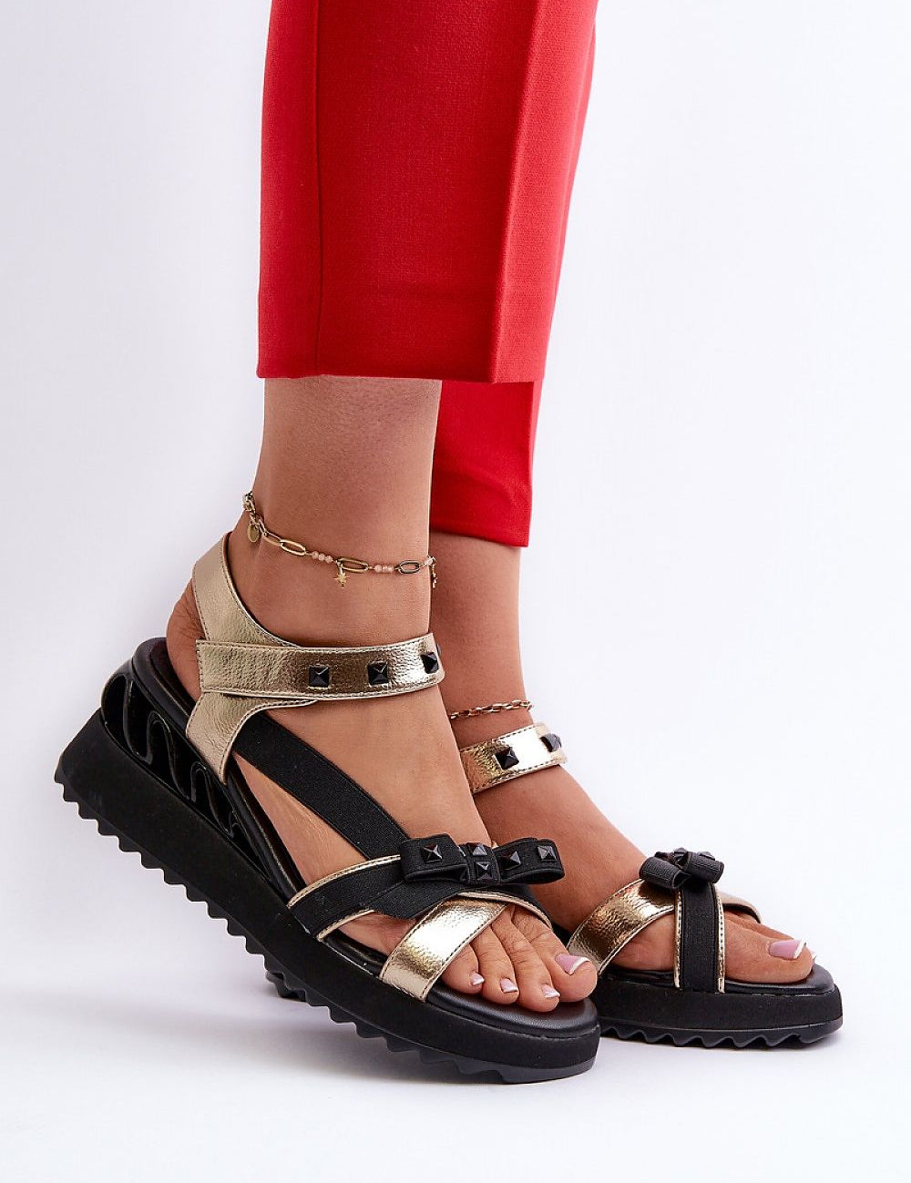 Aurelline Strap Bow Wedge Sandals with gold and black design, featuring bow detail, worn with red pants and ankle accessories