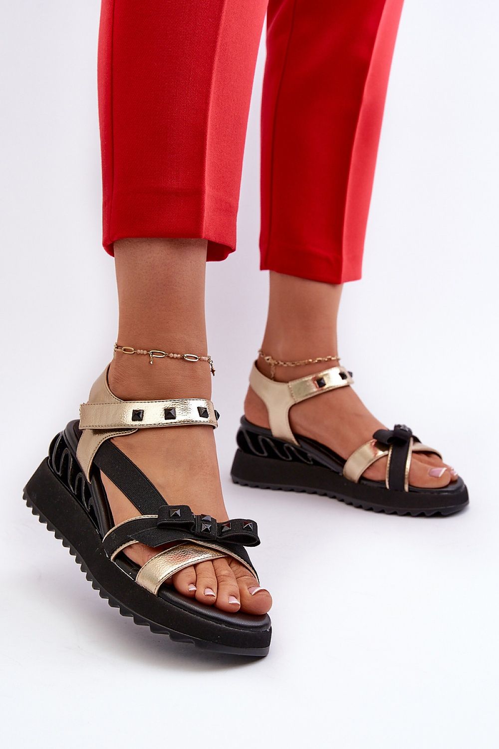 Woman wearing red pants and Aurelline Strap Bow Wedge Sandals with black soles and gold straps.