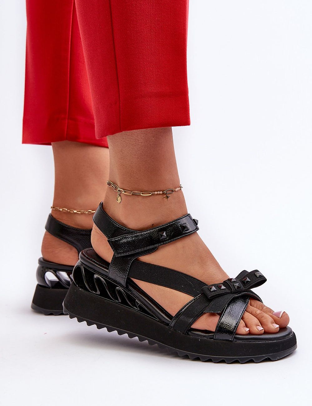 Woman wearing black Aurelline Strap Bow Wedge Sandals with red pants, featuring a delicate bow and Velcro strap for comfort.