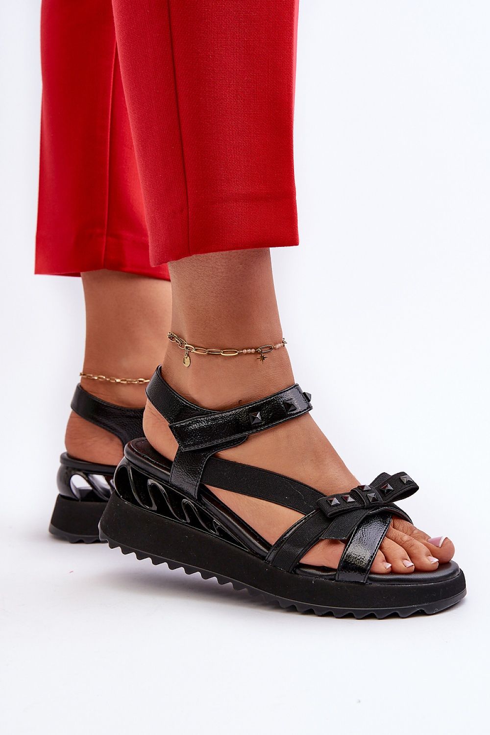 Woman wearing black Aurelline Strap Bow Wedge Sandals with red pants, featuring a delicate bow and Velcro strap for comfort.