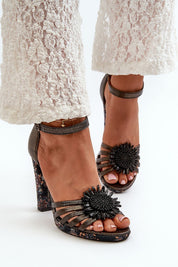 Women's sculpted leather high-heel sandals with ankle strap, floral embellishment, and lace-trimmed pants for elegant style.