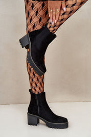 Black suede block heel ankle boots with side-zip, worn with patterned tights, showcasing style and elegance.