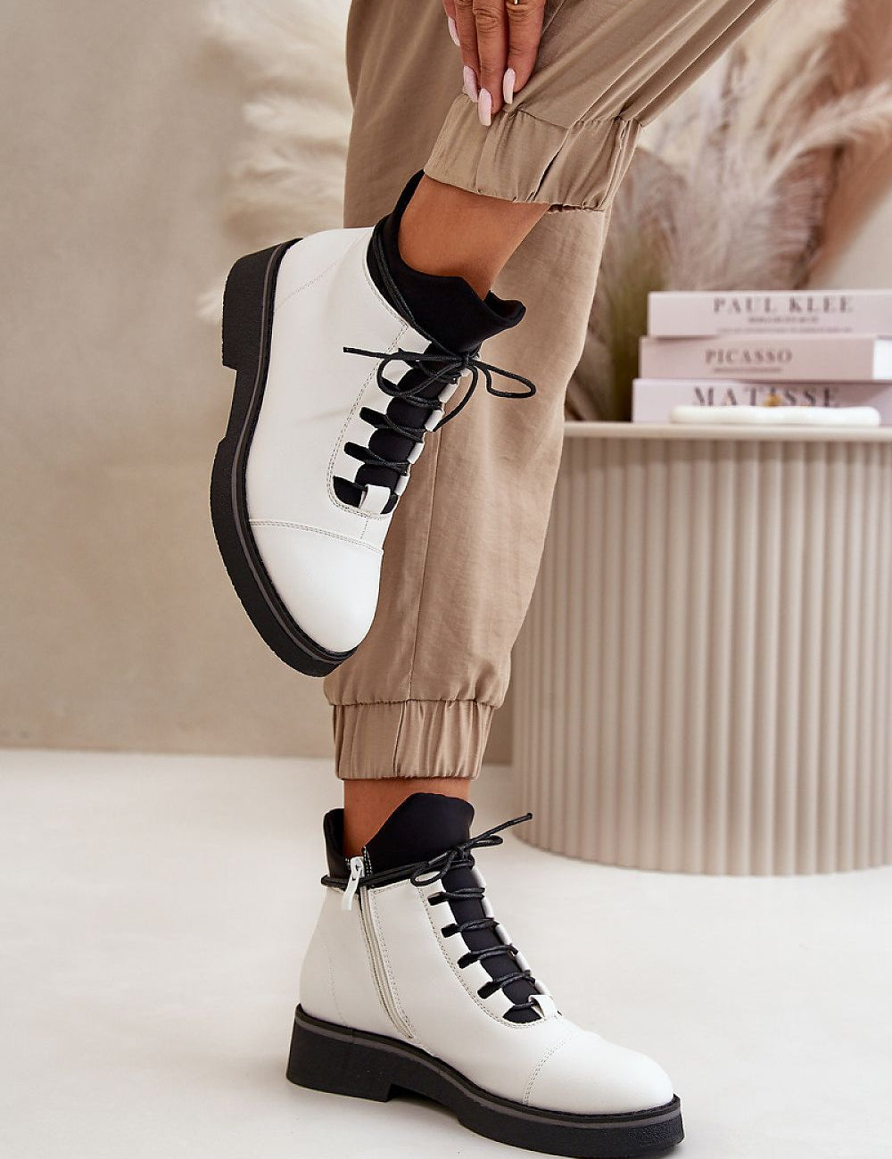 White eco-leather ankle boots with black laces, featuring a warm lining and flat heel, styled with beige joggers.
