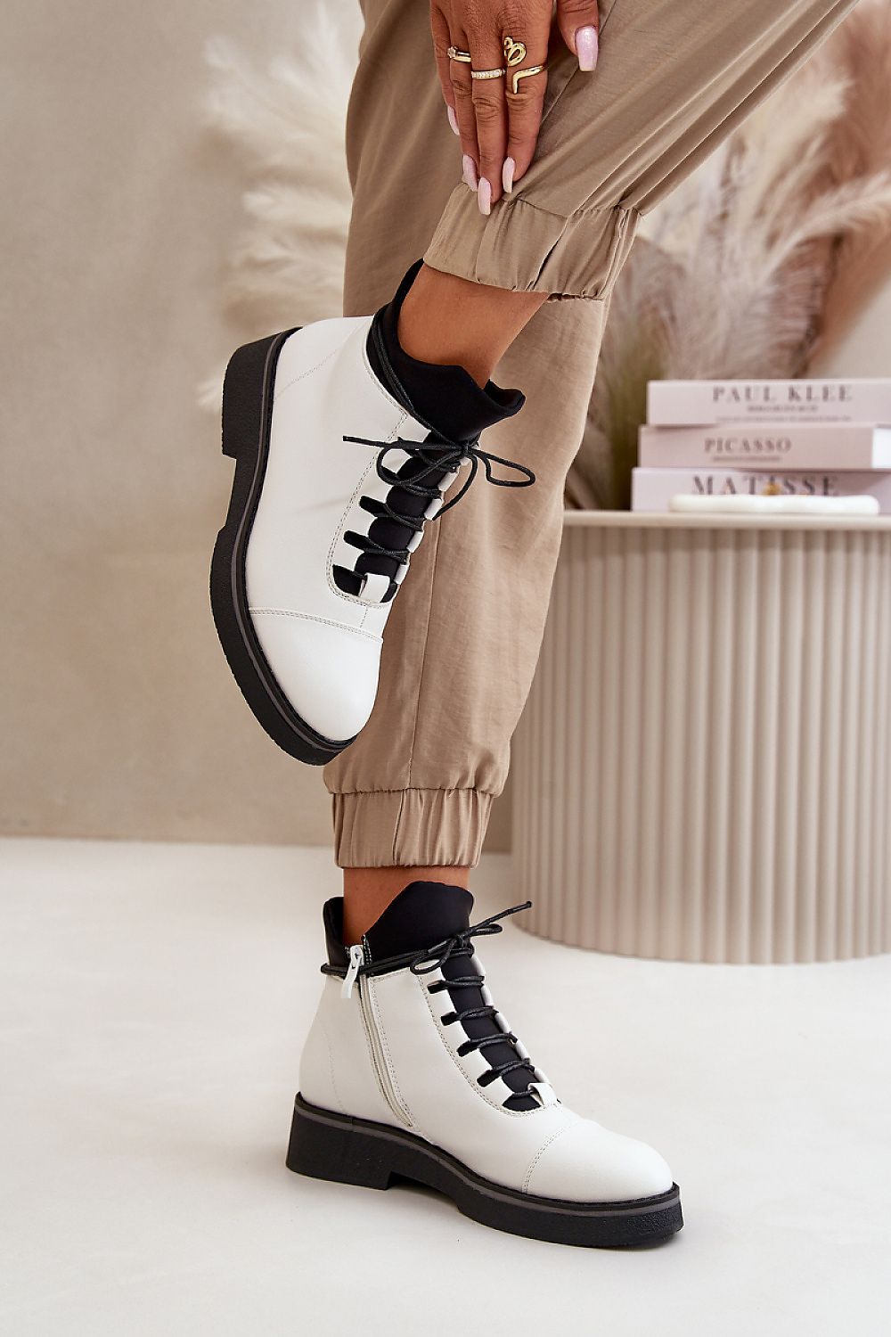 White eco-leather ankle boots with black laces, featuring a warm lining and flat heel, styled with beige joggers.
