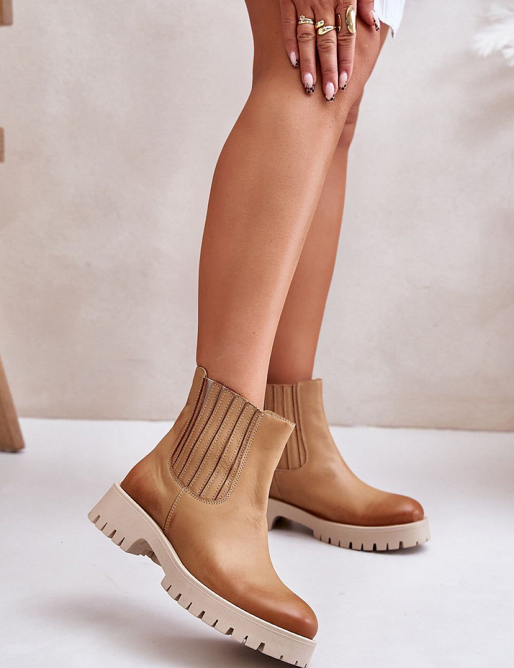 Tan ankle boots with chunky sole and ribbed elastic side panels, styled with a white outfit on model's legs