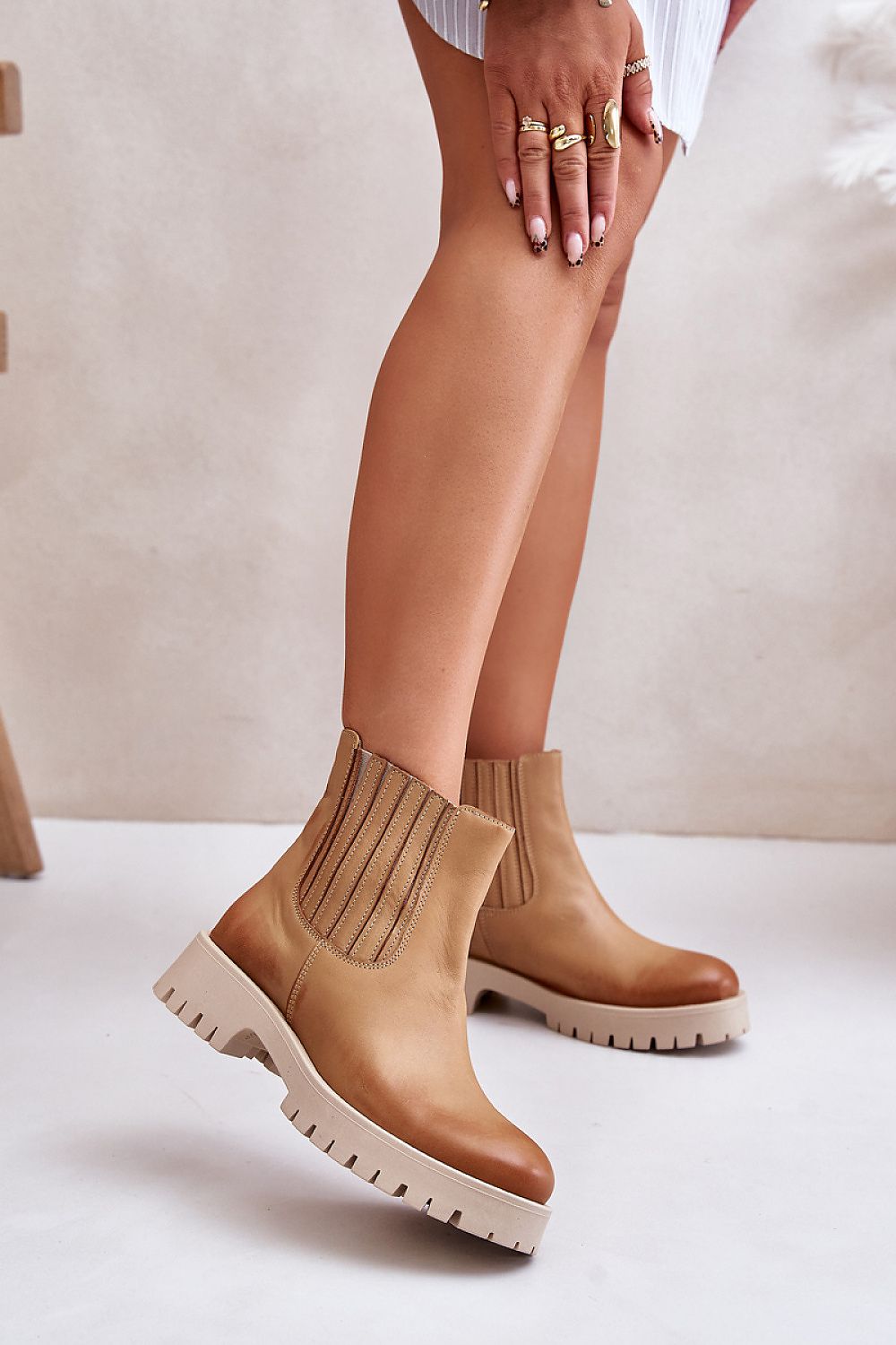 Tan ankle boots with chunky sole and ribbed elastic side panels, styled with a white outfit on model's legs