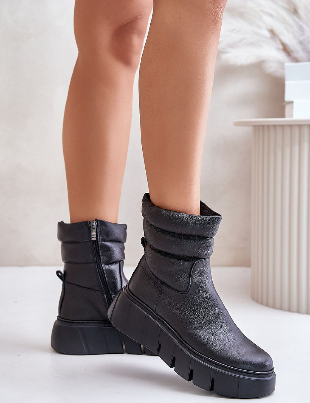 Black leather ankle boots with side zipper on white background, featuring a subtle wedge, grooved platform, and felt lining for comfort.