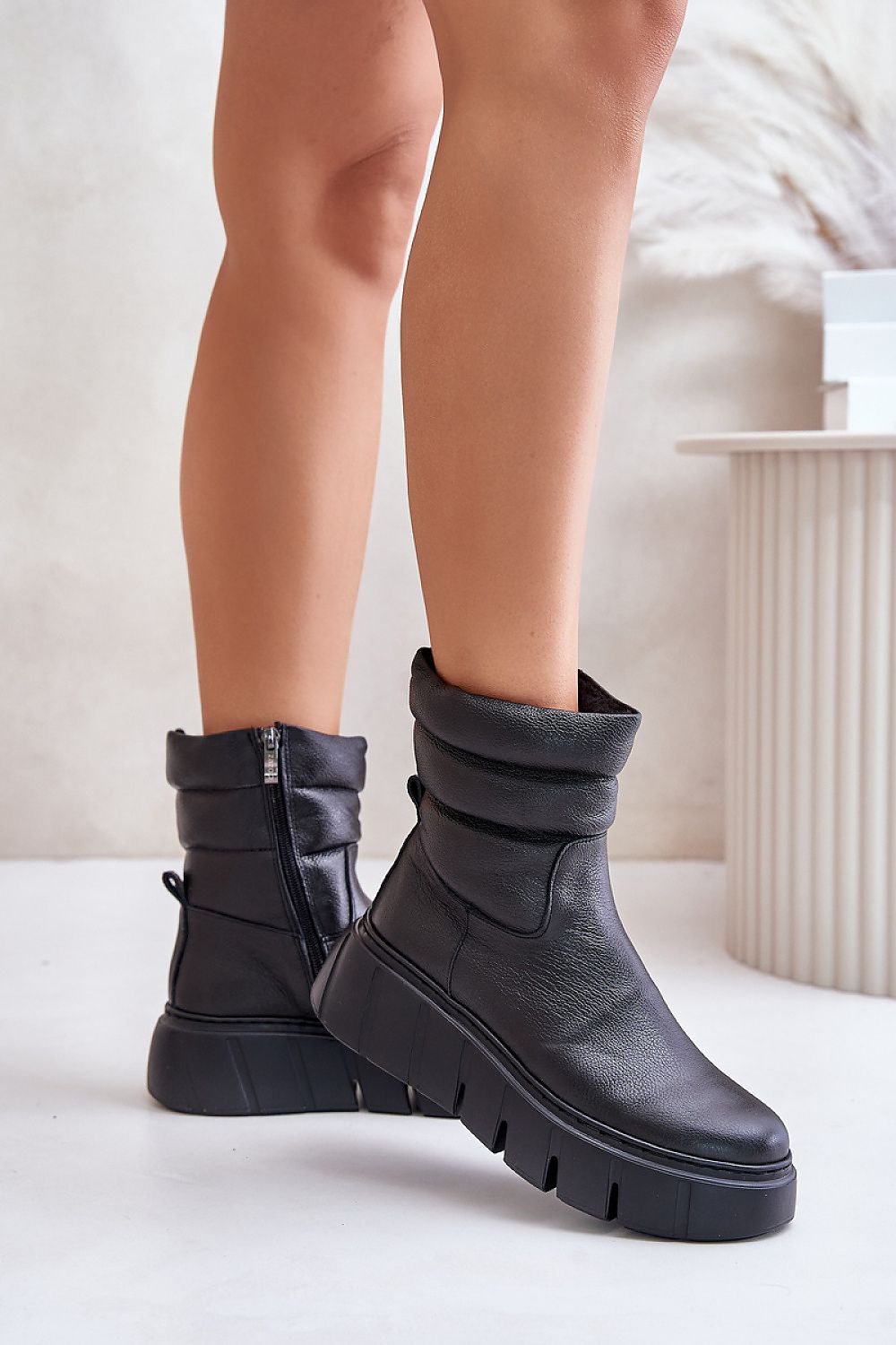 Black leather ankle boots with side zipper on white background, featuring a subtle wedge, grooved platform, and felt lining for comfort.