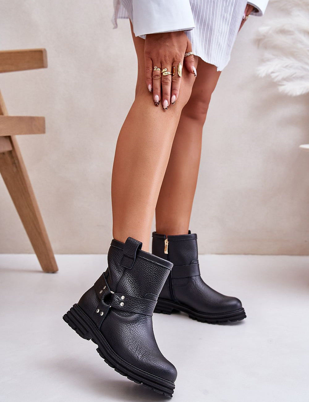 Woman wears black leather ankle boots with side zipper and buckle, showcasing elegant design on smooth white floor background.