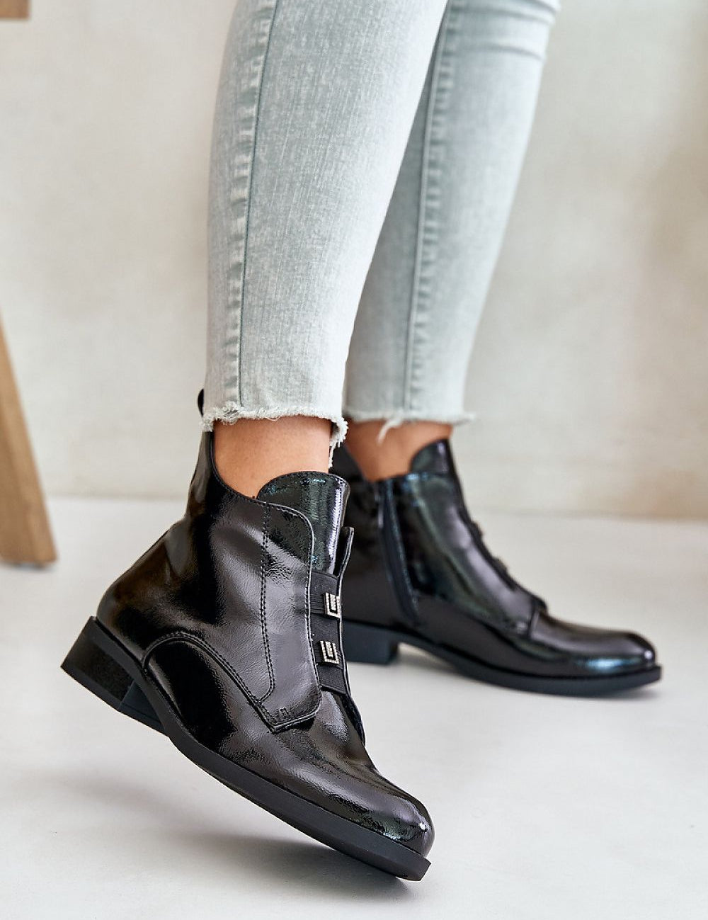 Woman wearing glossy black zip-up ankle boots with skinny jeans, showcasing a chic and modern footwear style.