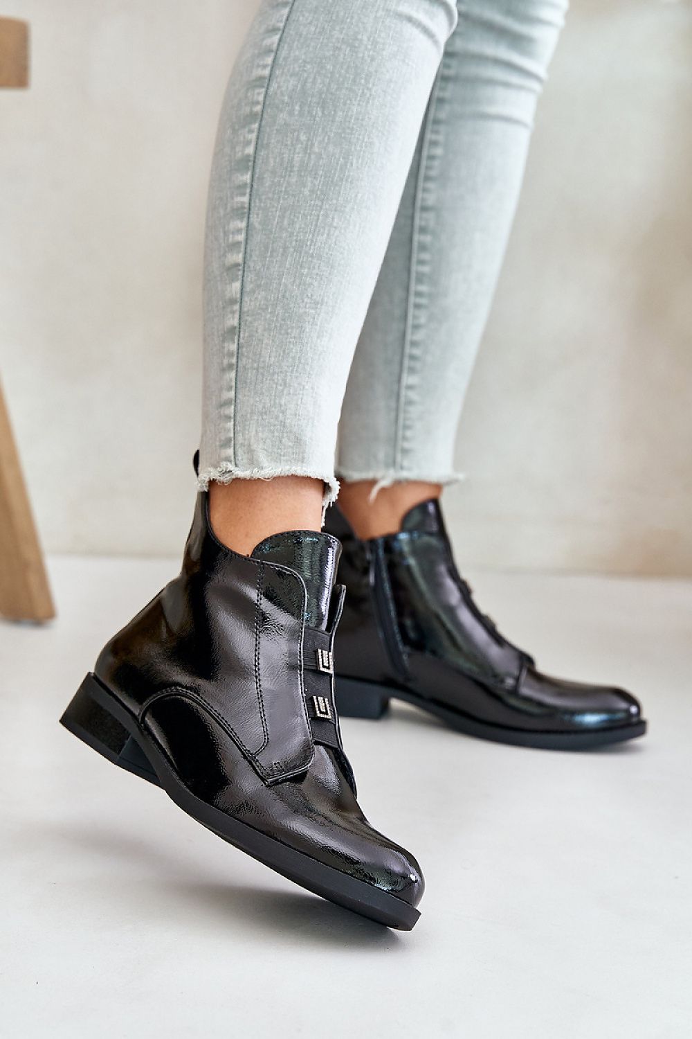 Woman wearing glossy black zip-up ankle boots with skinny jeans, showcasing a chic and modern footwear style.