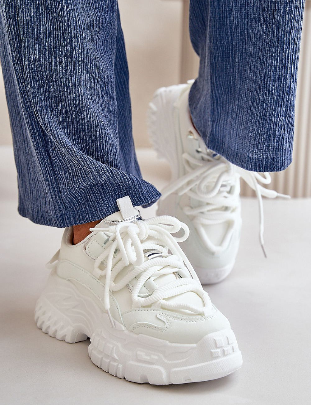 Person wearing white Varetta Chunky Lace-Up Sneakers with thick platform sole and blue pants, showcasing bold silhouette and stylish design.