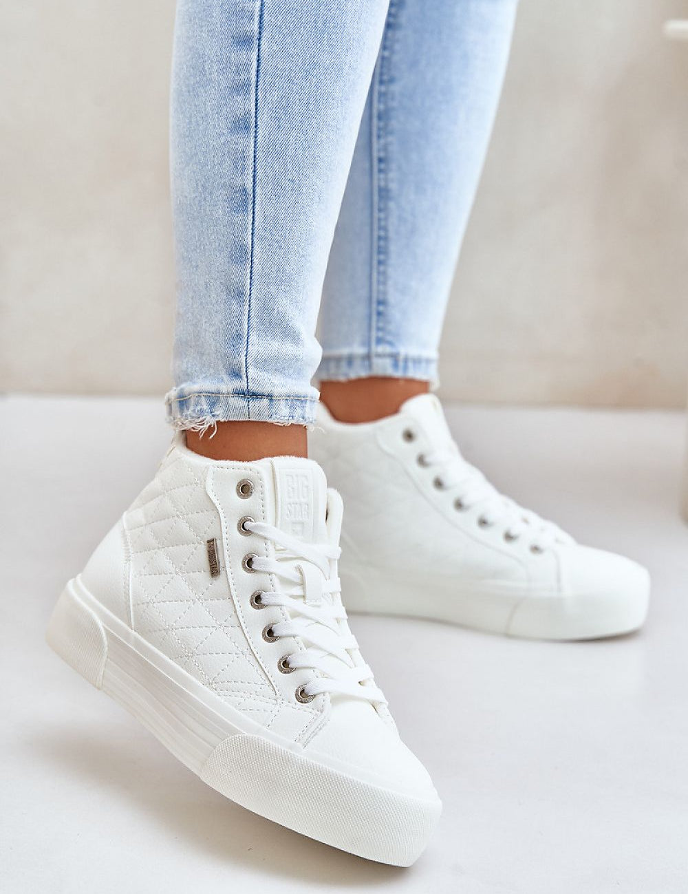 White Elbrina insulated winter sneakers with high-top design, decorative stitching, and secure lacing system, worn with light denim jeans.