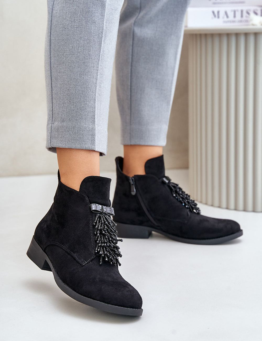Woman wearing Evarine Frontglow eco-suede ankle boots with embellishment, gray pants, eco-friendly, insulated interior for warmth.