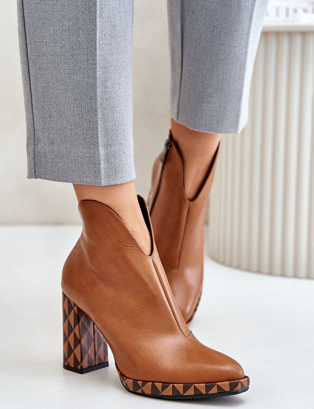 Brown leather ankle boots with geometric heels, styled with gray pants, featuring almond-shaped toe and side zipper.