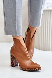 Brown leather ankle boots with geometric heels, styled with gray pants, featuring almond-shaped toe and side zipper.