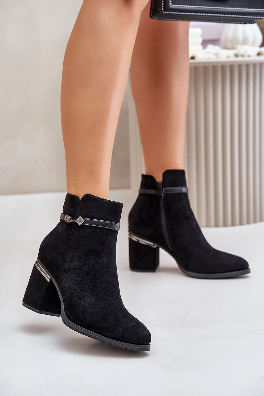Black suede ankle boots with side zipper and decorative strap, featuring chunky heel and almond toe, styled for autumn wear.