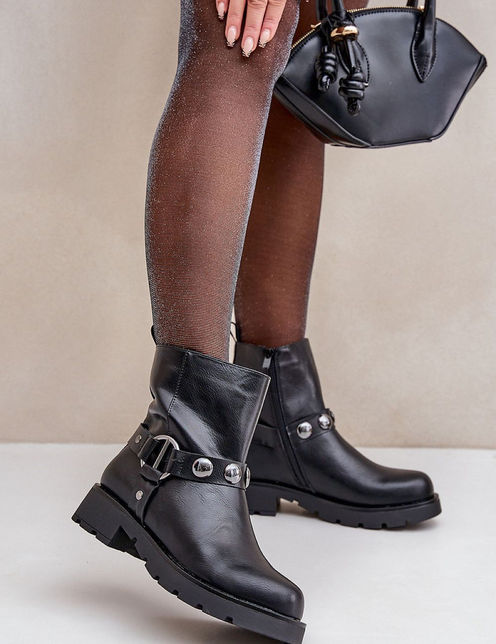 Woman wearing Varita Everyday Ankle Boots in black eco leather with decorative straps, holding a handbag.