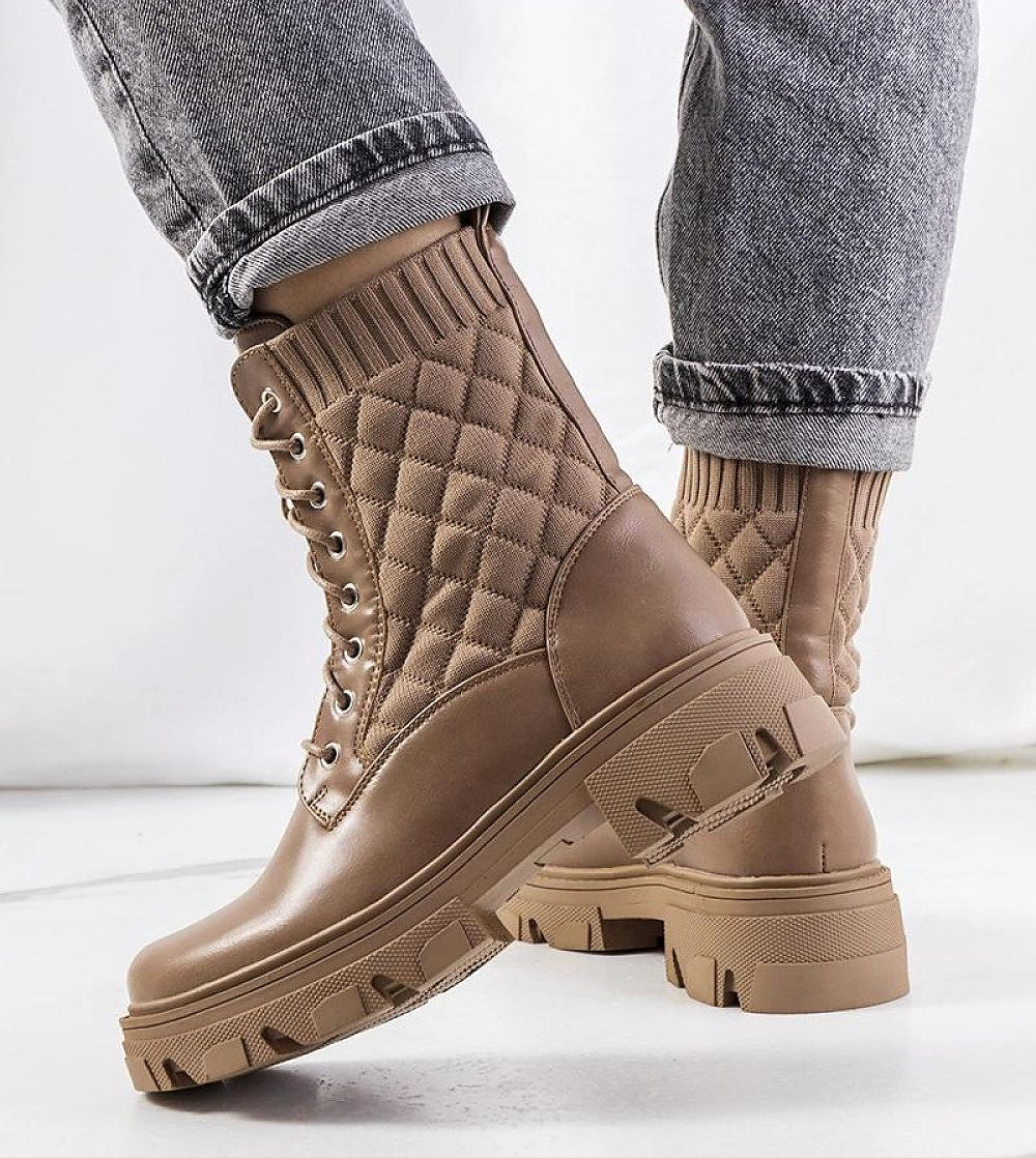 Taupe quilted ankle boots with high trekking-style sole and lace-up closure, paired with cuffed jeans for a stylish look.
