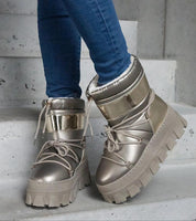 Golden lacquered platform snow boots with lace-up closure and chunky sole, designed for bold winter fashion and all-weather use.