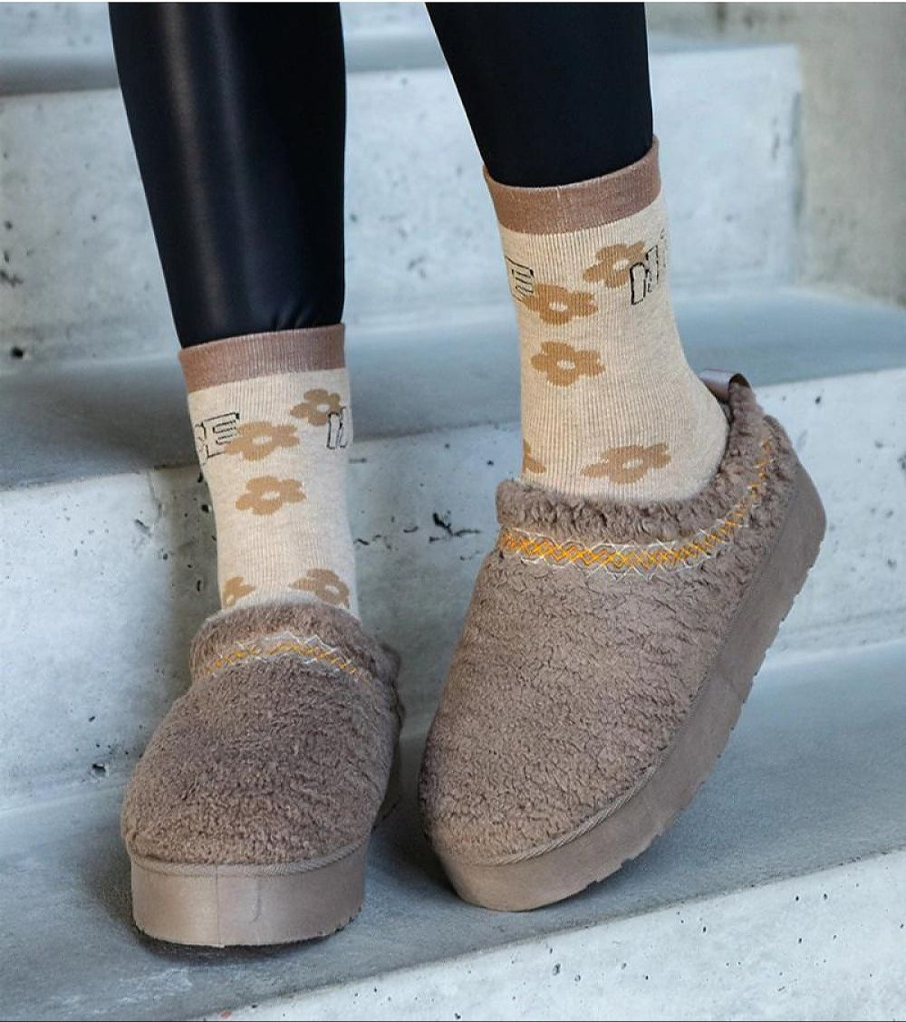 Cozy brown slip-on winter boots with embroidered details and floral socks on concrete steps.