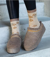 Cozy brown slip-on winter boots with embroidered details and floral socks on concrete steps.