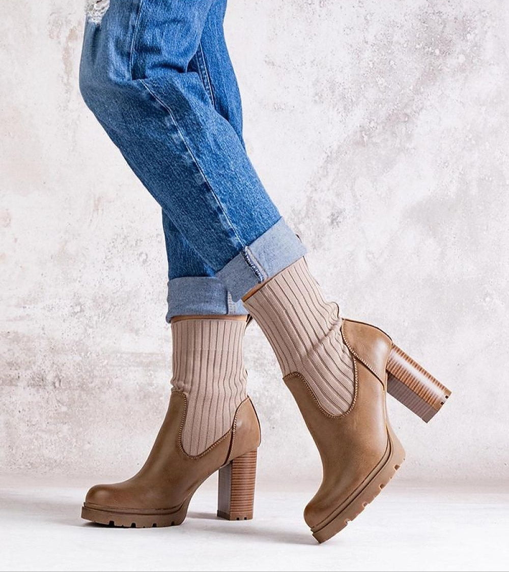Brown ankle boots with ribbed socks and block heel worn with cuffed jeans on textured background.