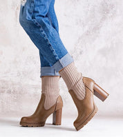 Brown ankle boots with ribbed socks and block heel worn with cuffed jeans on textured background.