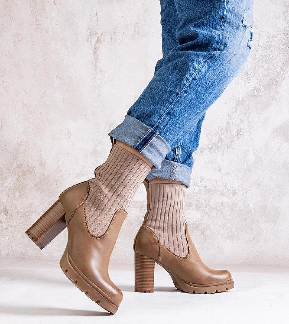 Person wearing brown stiletto ankle boots with ribbed socks and rolled-up jeans, showcasing a stylish fall fashion look.