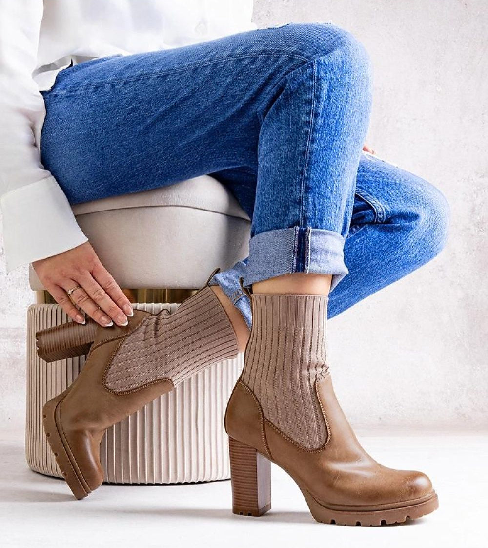 Woman wearing brown ankle boots with knit socks, sitting on ottoman, showcasing chic autumn style with jeans.