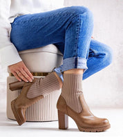 Woman wearing brown ankle boots with knit socks, sitting on ottoman, showcasing chic autumn style with jeans.