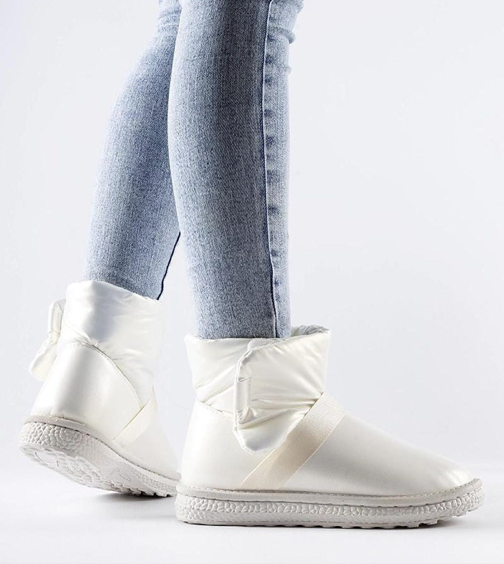 White glossy Velcro snow boots with platform, worn with blue jeans, highlighting winter elegance and practical Velcro closure.
