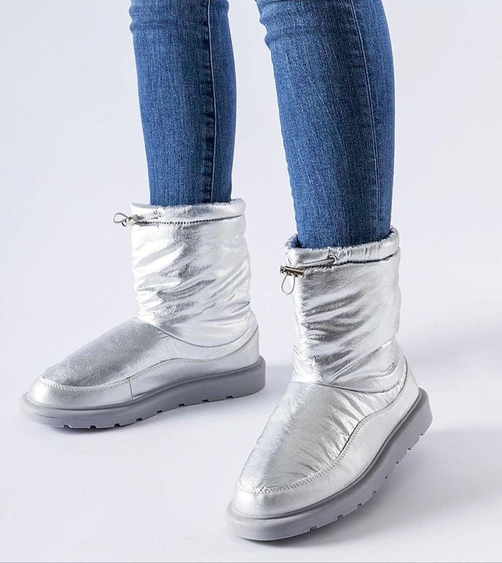 Person wearing silver Sylverra Slip-On Winter Snow Boots with jeans, featuring sleek design and waterproof sole for icy surfaces.