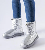 Person wearing silver Sylverra Slip-On Winter Snow Boots with jeans, featuring sleek design and waterproof sole for icy surfaces.