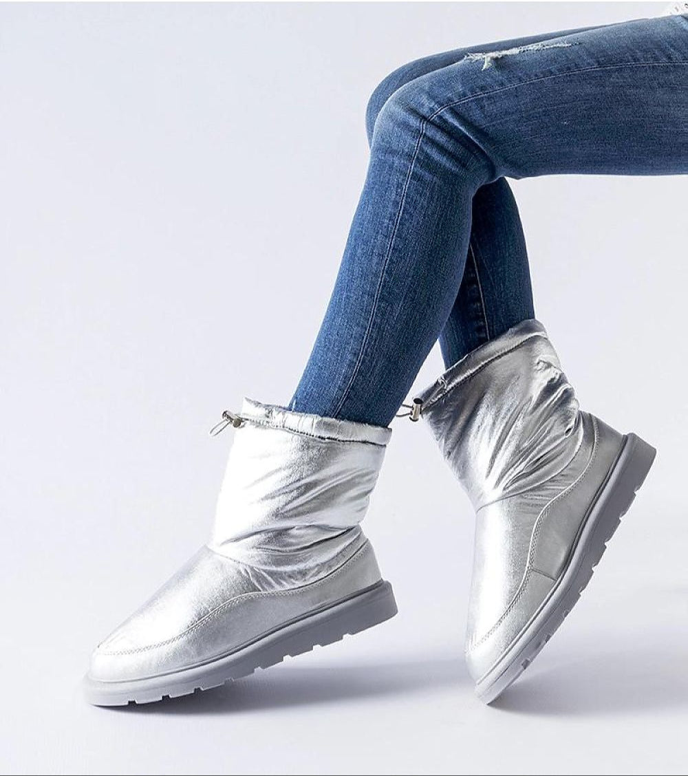 Silver slip-on winter snow boots with round toe and waterproof sole, worn with jeans, offering warmth and style for icy conditions.