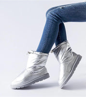 Silver slip-on winter snow boots with round toe and waterproof sole, worn with jeans, offering warmth and style for icy conditions.