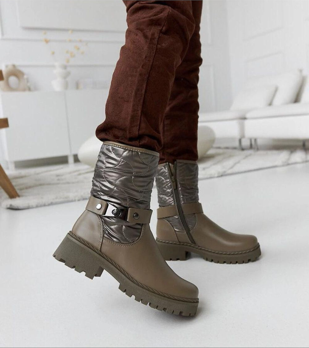 Renvara Strap Detail Ankle Boots with decorative strap and side zipper, styled with brown pants in a modern living room setting.
