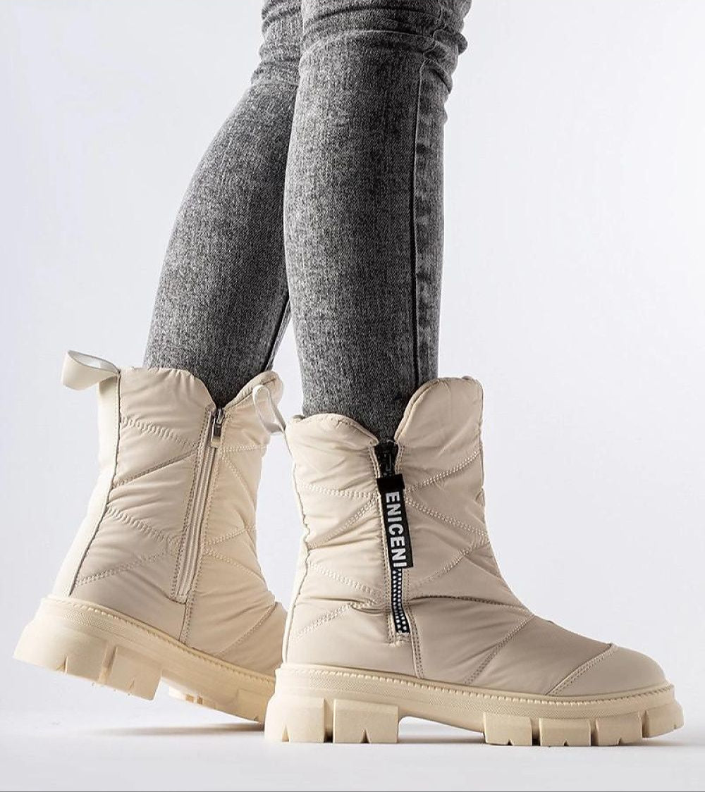 Person wearing white quilted snow boots with side zipper and high shaft for winter insulation, standing on light background.
