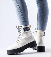 White ankle boots with black thick soles and laces, worn with blue jeans, showcasing a stylish and rugged look for casual wear.