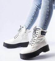 White ankle boots with black soles and laces, worn with light blue jeans. Modern winter footwear for style and comfort.