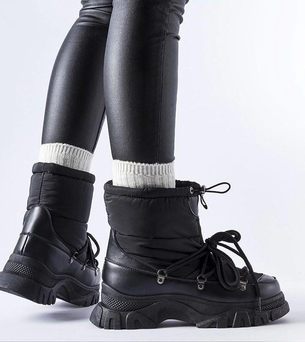 Side view of black Eldarien Lace-Up Snow Boots with rugged soles, worn with black leggings and white socks, highlighting winter style.