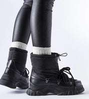 Side view of black Eldarien Lace-Up Snow Boots with rugged soles, worn with black leggings and white socks, highlighting winter style.