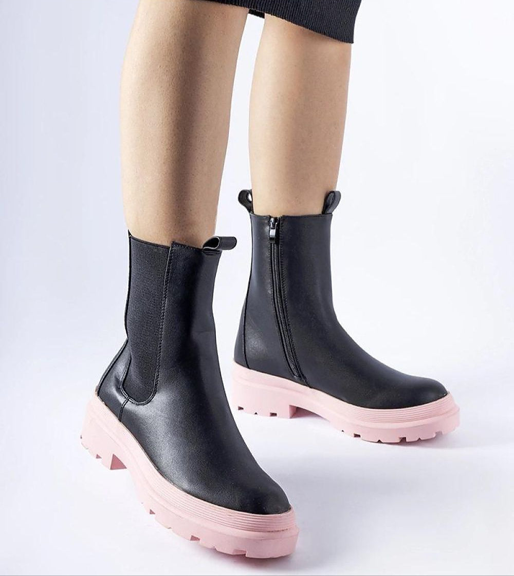 Black ankle boots with pink soles and side zippers, worn with a skirt, showcasing modern design and comfort for winter fashion.
